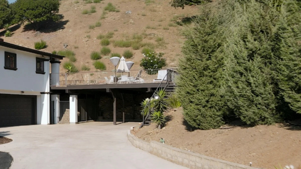 Hillside home with driveway, retaining wall and mature evergreen screening